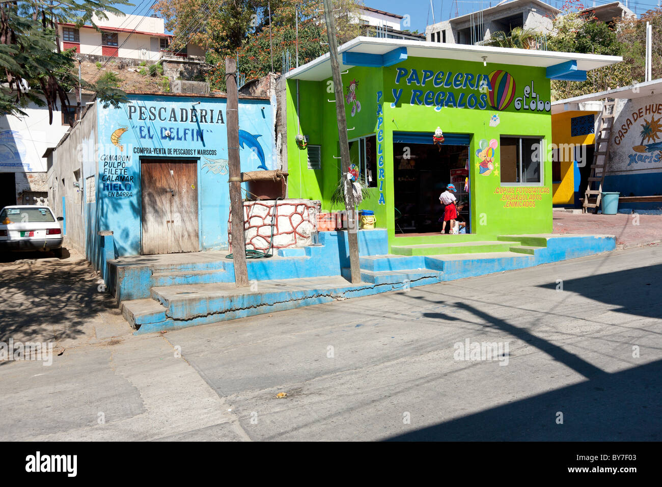 Dos pequeñas tiendas pintadas en tonos brillantes de verde lima y turquesa compiten por la atención en una calle de Puerto Angel, México Foto de stock