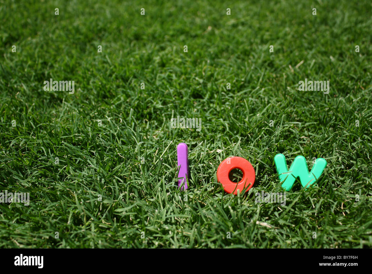 La palabra 'bajo' escrito en letras de plástico multicolor, sobre la hierba verde Foto de stock