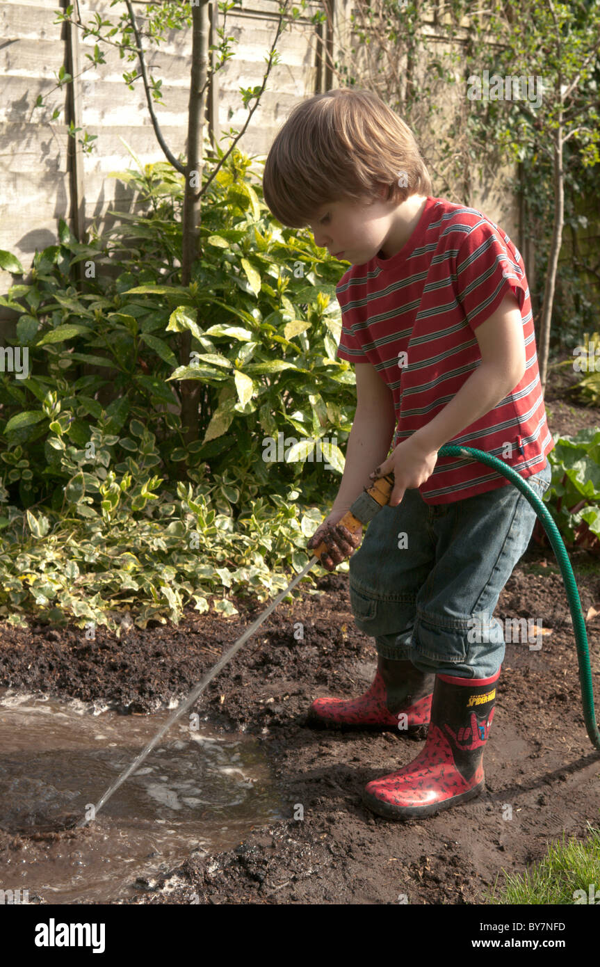 Niño jugando con manguera haciendo un charco de lodo y en el jardín de  atrás. Cuatro-año-viejo Fotografía de stock - Alamy
