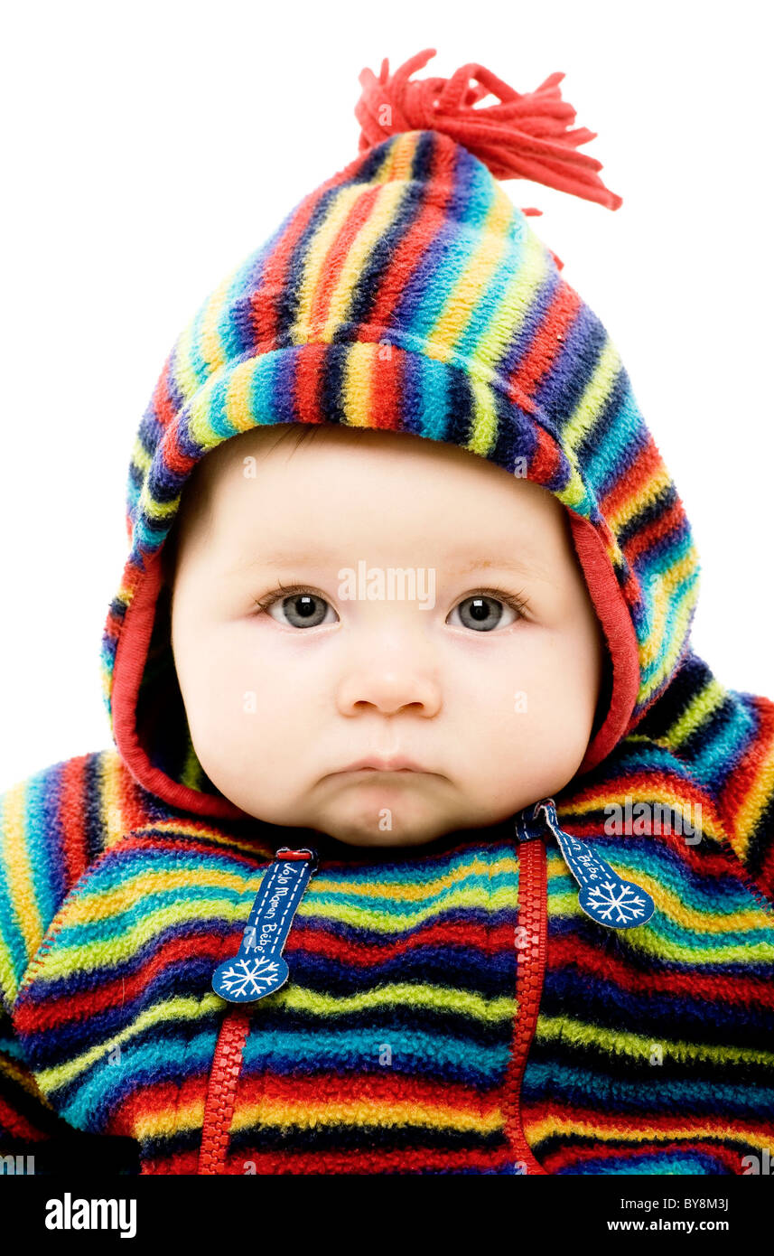 Fotografía de un bebé caucásico con una expresión grumosa, mirando directamente a la cámara, con un traje de rayas de colores brillantes con la capucha hacia arriba. Foto de stock