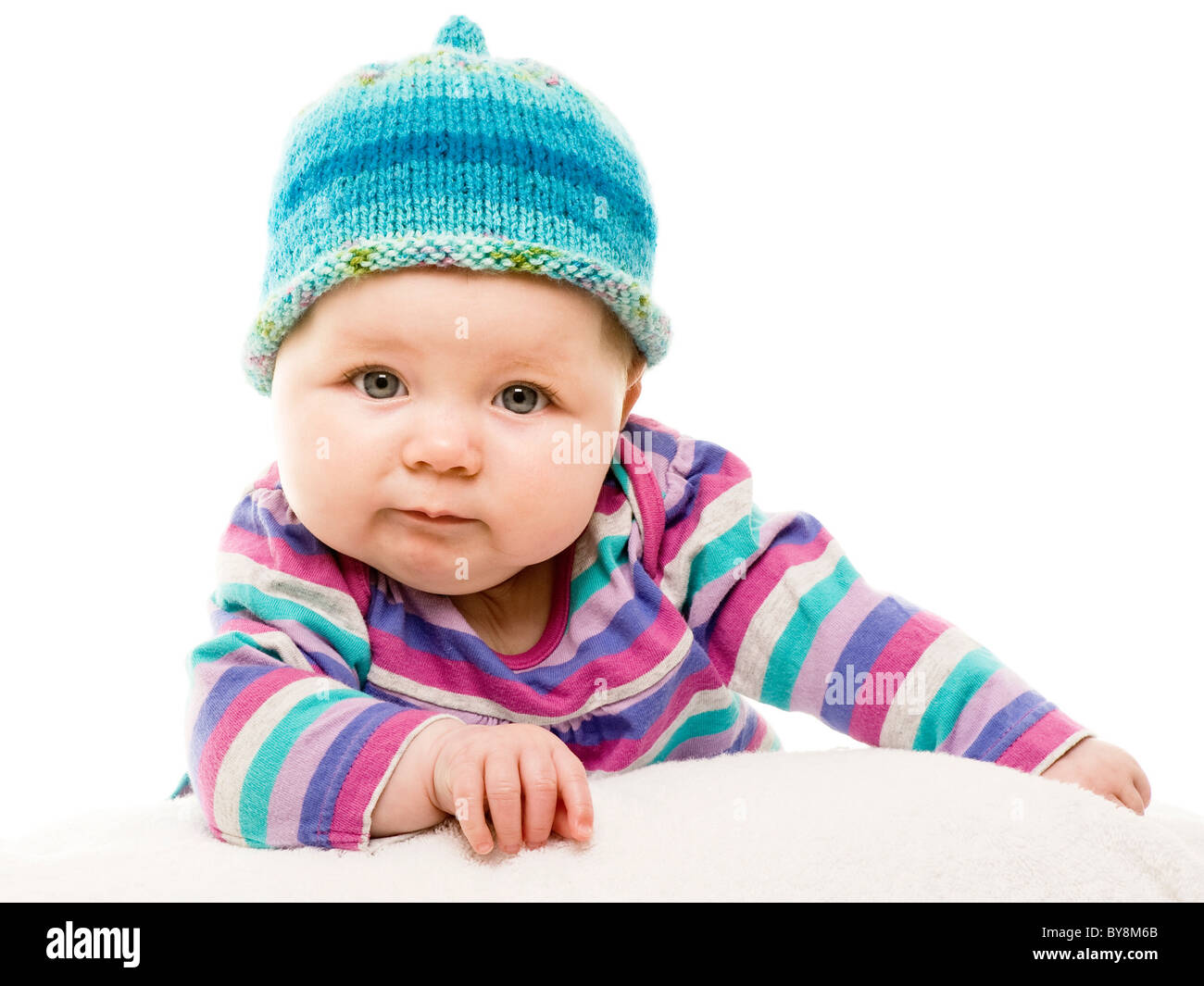 Tiro de cabeza y hombros de un bebé caucásico con ojos verdes, vestido con un traje de rayas de colores brillantes y sombrero de punto de mano turquesa, Foto de stock