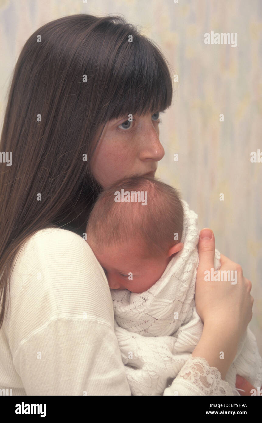 Infeliz joven madre sosteniendo a su bebé recién nacido Foto de stock