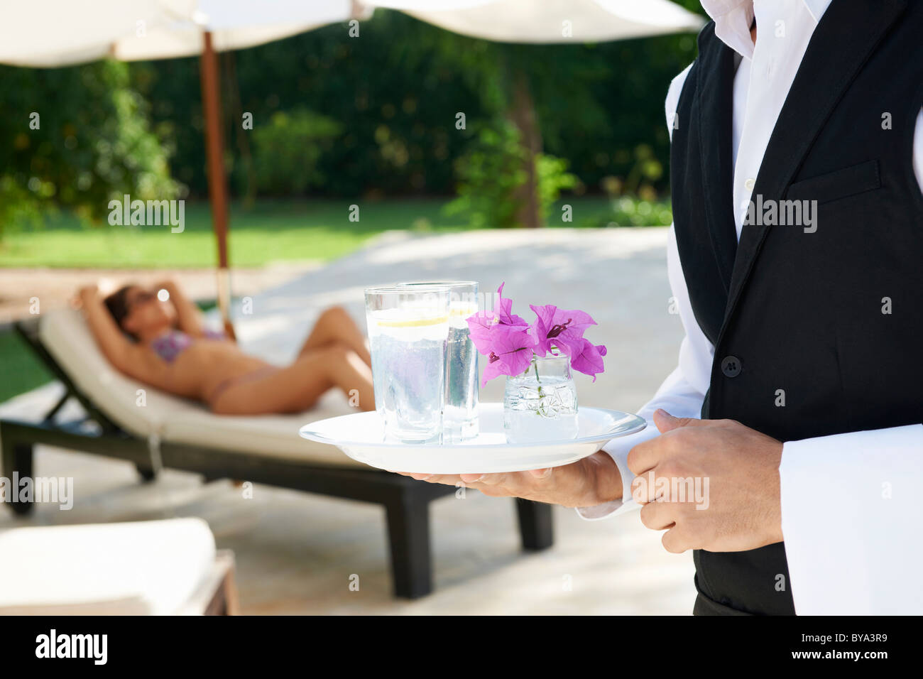 Hotel camarero sosteniendo la bandeja por la piscina del hotel Foto de stock