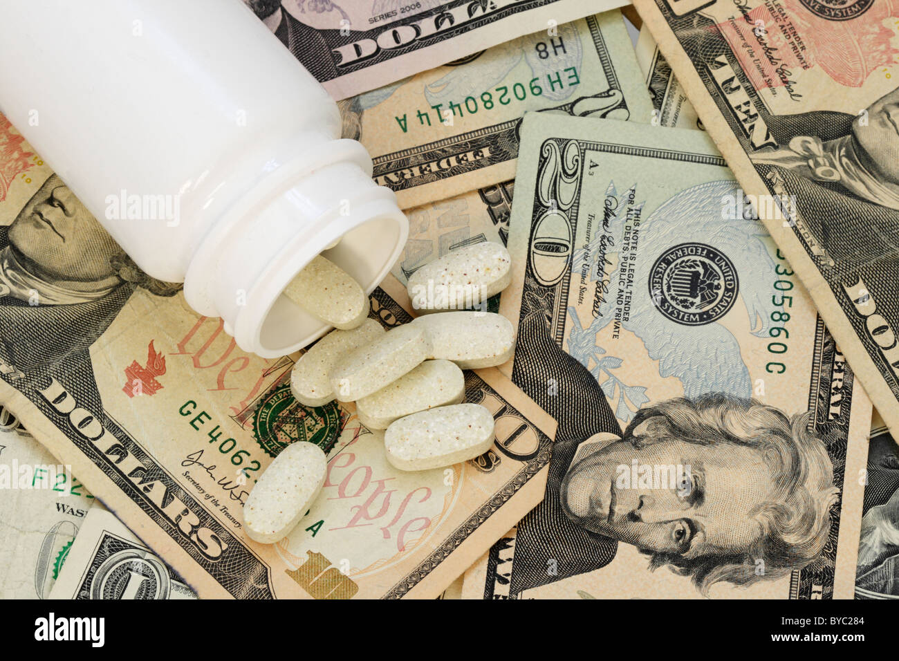 Pastilla blanca frasco de tabletas de pastillas de drogas derramando sobre un fondo de dinero de papel estadounidenses ilustrando el alto costo de los medicamentos Foto de stock