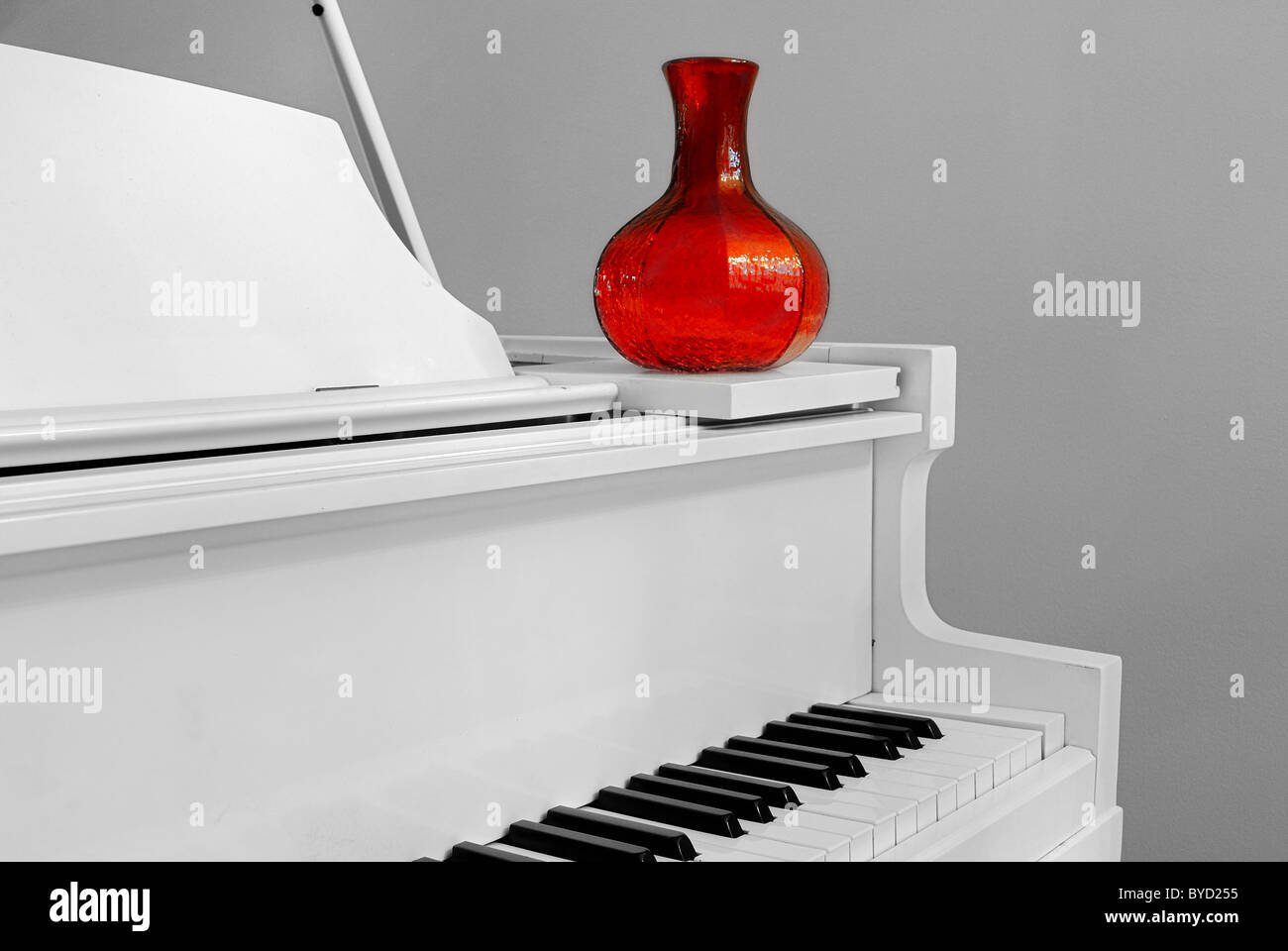 Esquina de un piano con un jarrón de color rojo en el interior de una casa. Foto de stock
