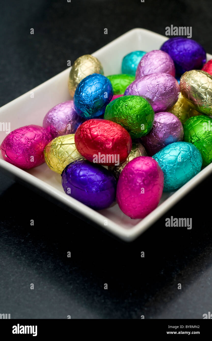 Una pequeña selección de mini huevos de chocolate en un plato blanco sobre una superficie negra Foto de stock