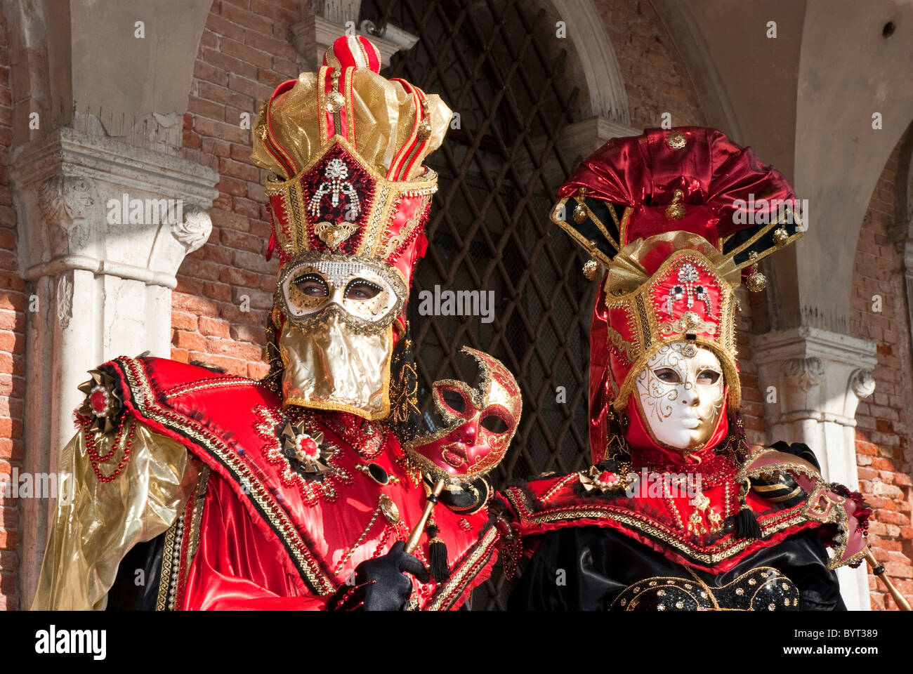Un par de máscaras venecianas durante el carnaval con disfraz rojo y dorado.  Posando bajo un pórtico Fotografía de stock - Alamy