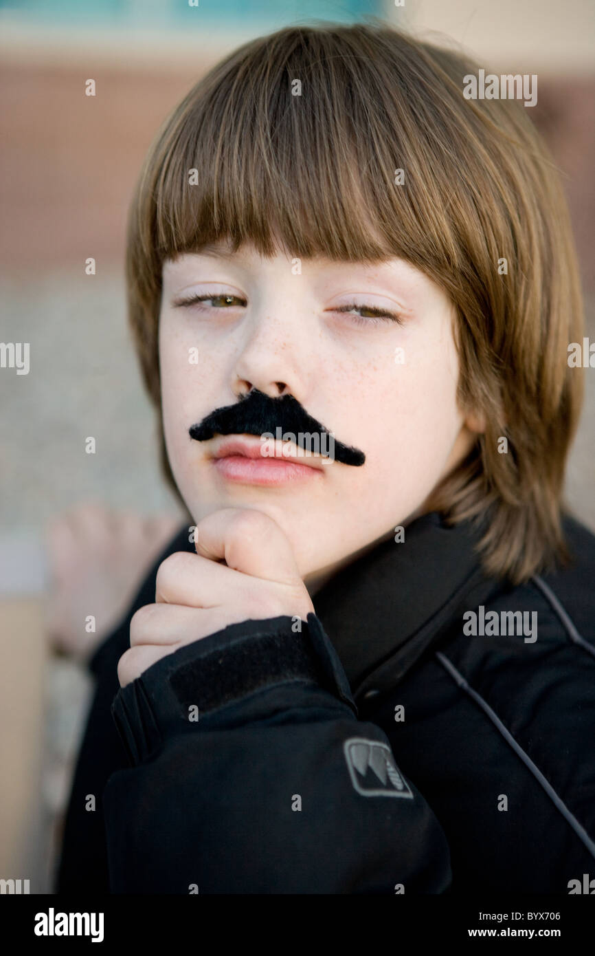 Un niño de ocho años vistiendo un pretender el bigote con la mano en la barbilla, actuando como un hombre adulto en una profunda reflexión. Foto de stock