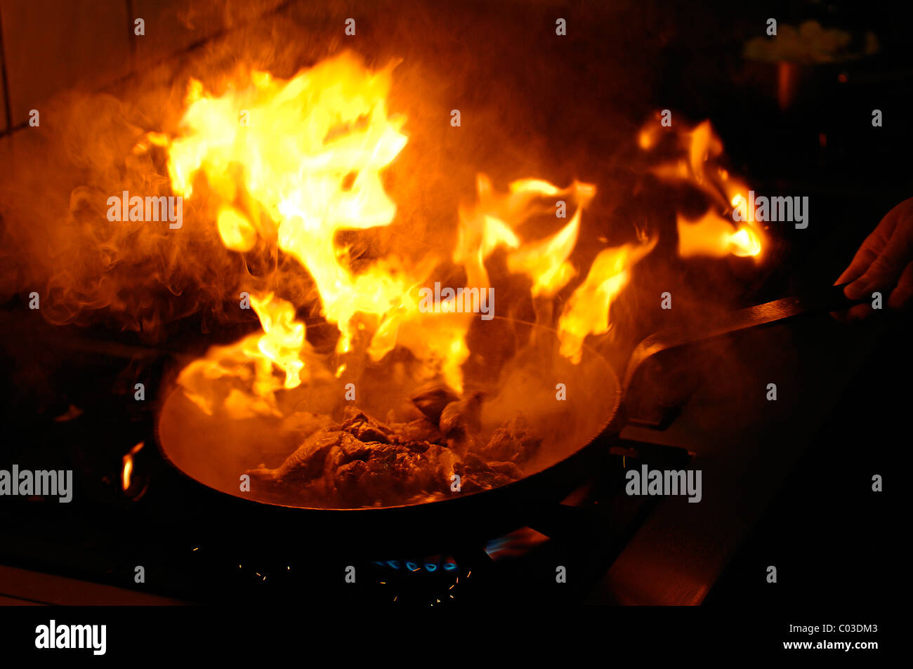 Llama explosivo en una sartén con carne frita en una estufa de gas con la grasa que está demasiado caliente. Foto de stock