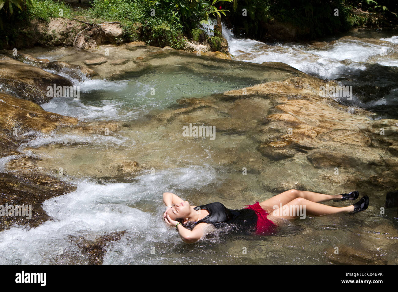 Joven turista se relaja en una piscina de poca profundidad de agua en las Cataratas del río Dunn en Jamaica. Foto de stock