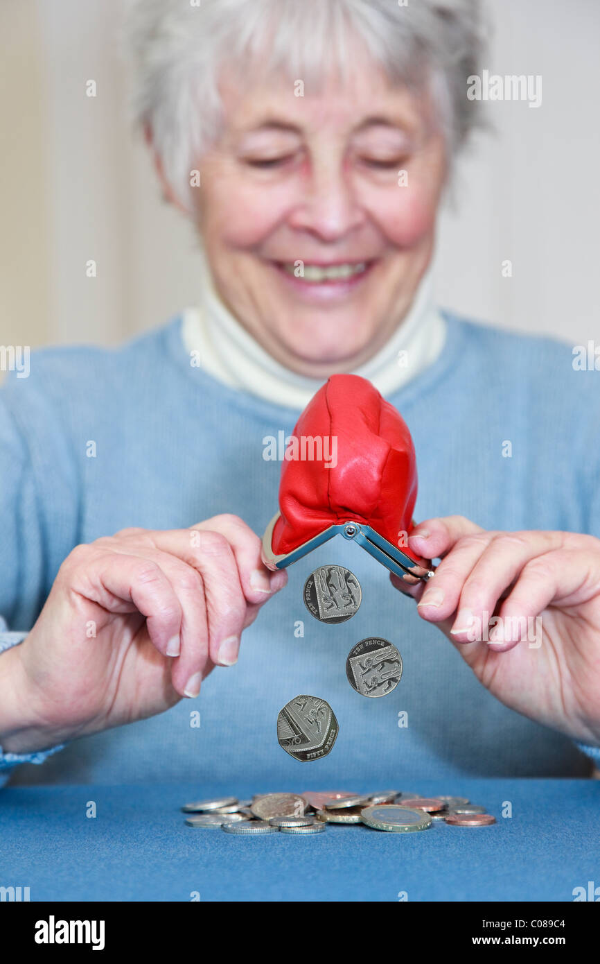 Compuesto de una anciana pensionista rica mujer jubilada de OAP con una expresión feliz vaciando un montón de monedas de un monedero. Inglaterra, Reino Unido Foto de stock