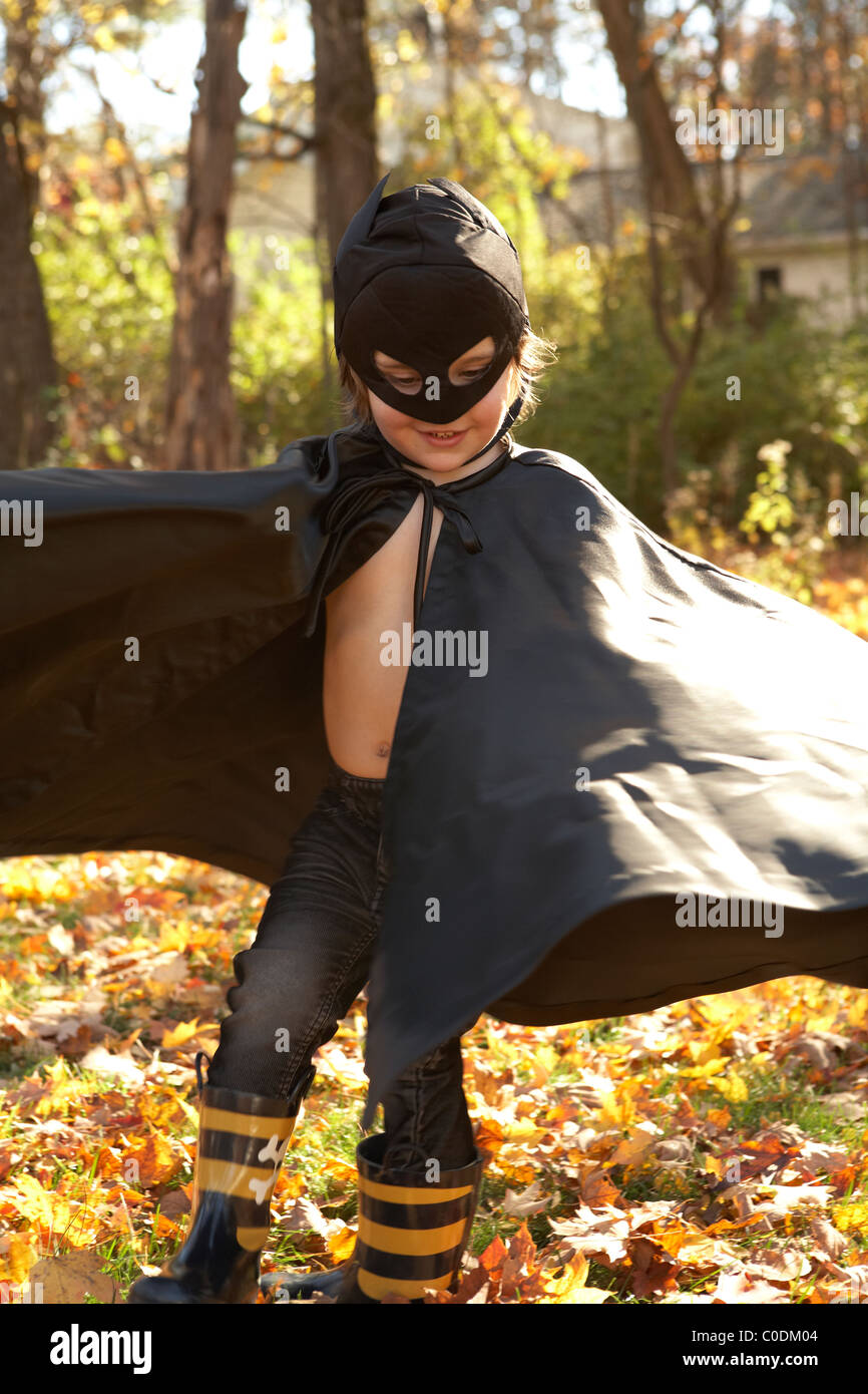 Kid vestido como Batman jugando en las hojas Foto de stock