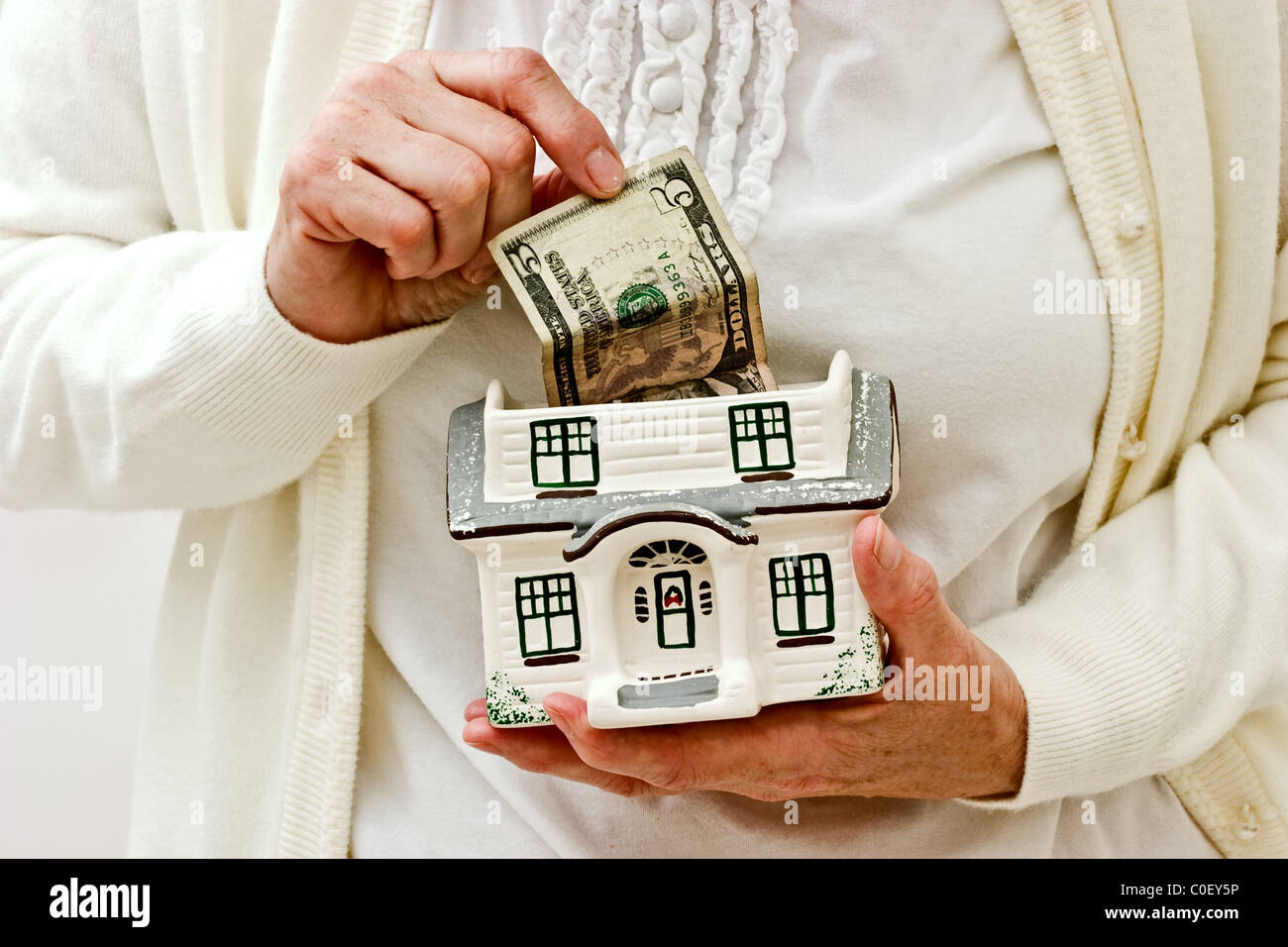 Mujer tirando el dinero de la parte superior de una pequeña casa de cerámica Foto de stock