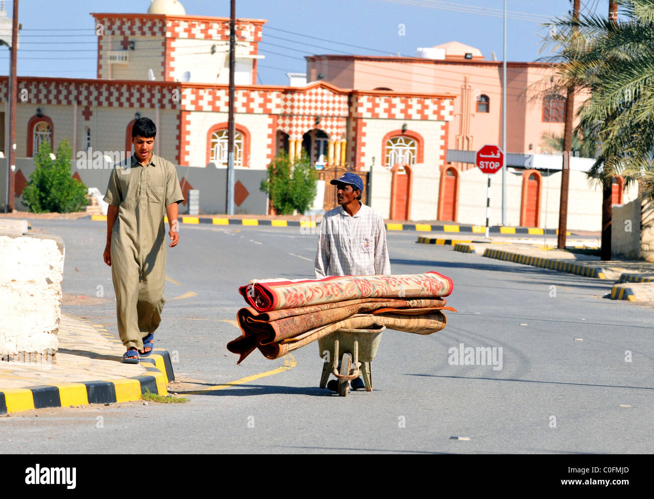 Escena de una calle Al Rustaq, dos hombres con rollos de alfombras. La Sultanía de Omán. Foto de stock