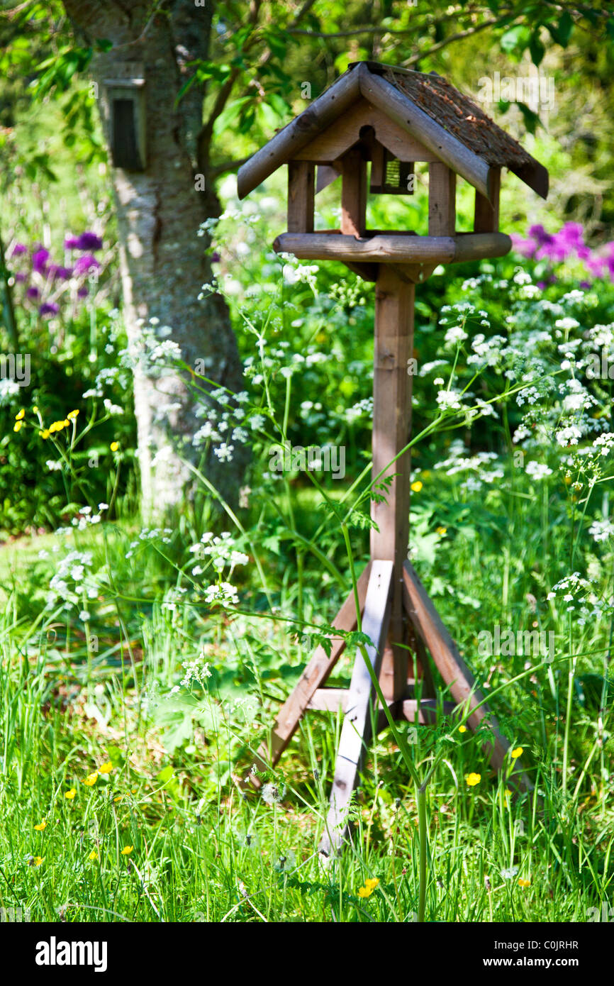 Una bonita mesa de madera rústica o alimentador de aves entre bordes florales o camas en un país inglés jardín en verano Foto de stock