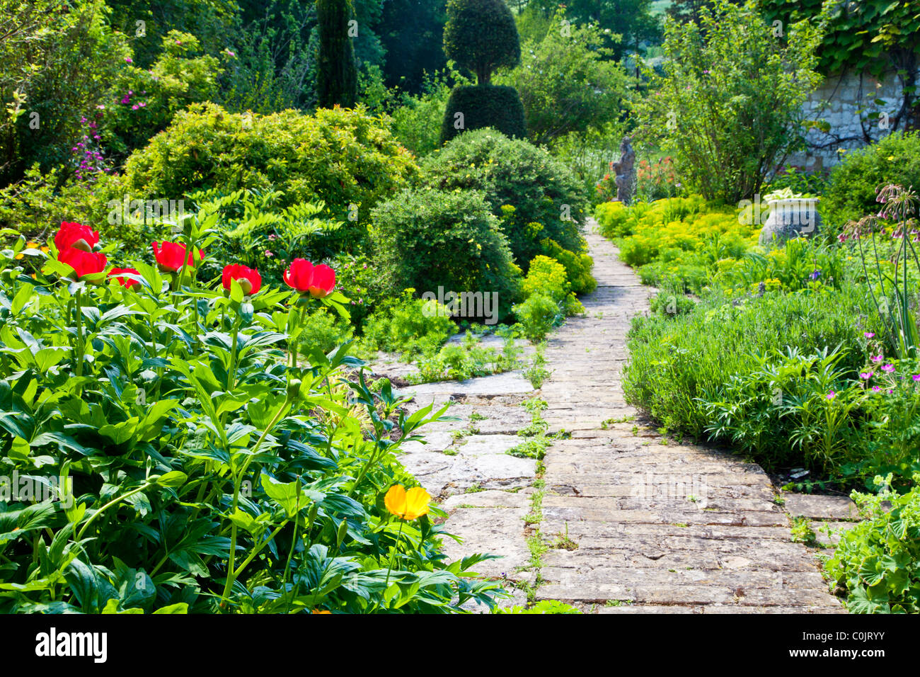 Un jardín pavimentado camino entre los arbustos y los bordes florales en inglés un país jardín en verano Foto de stock