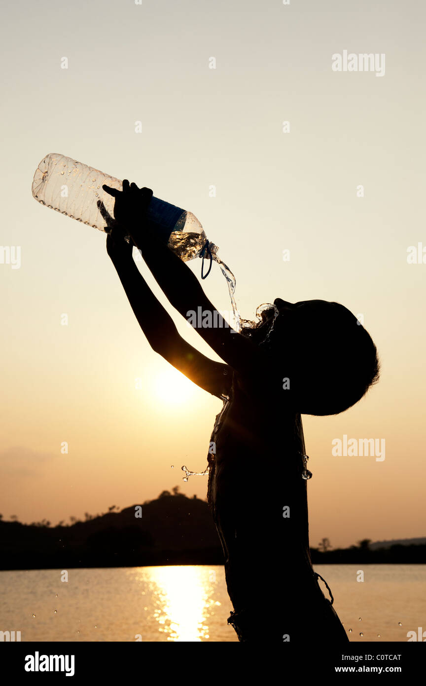 Niño Indio beber agua mineral de botella de plástico al atardecer. Silueta. La India Foto de stock