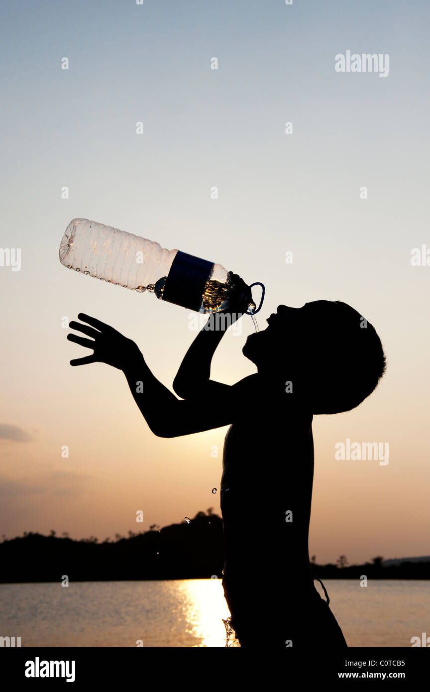 Niño Indio beber agua mineral de botella de plástico al atardecer. Silueta. La India Foto de stock
