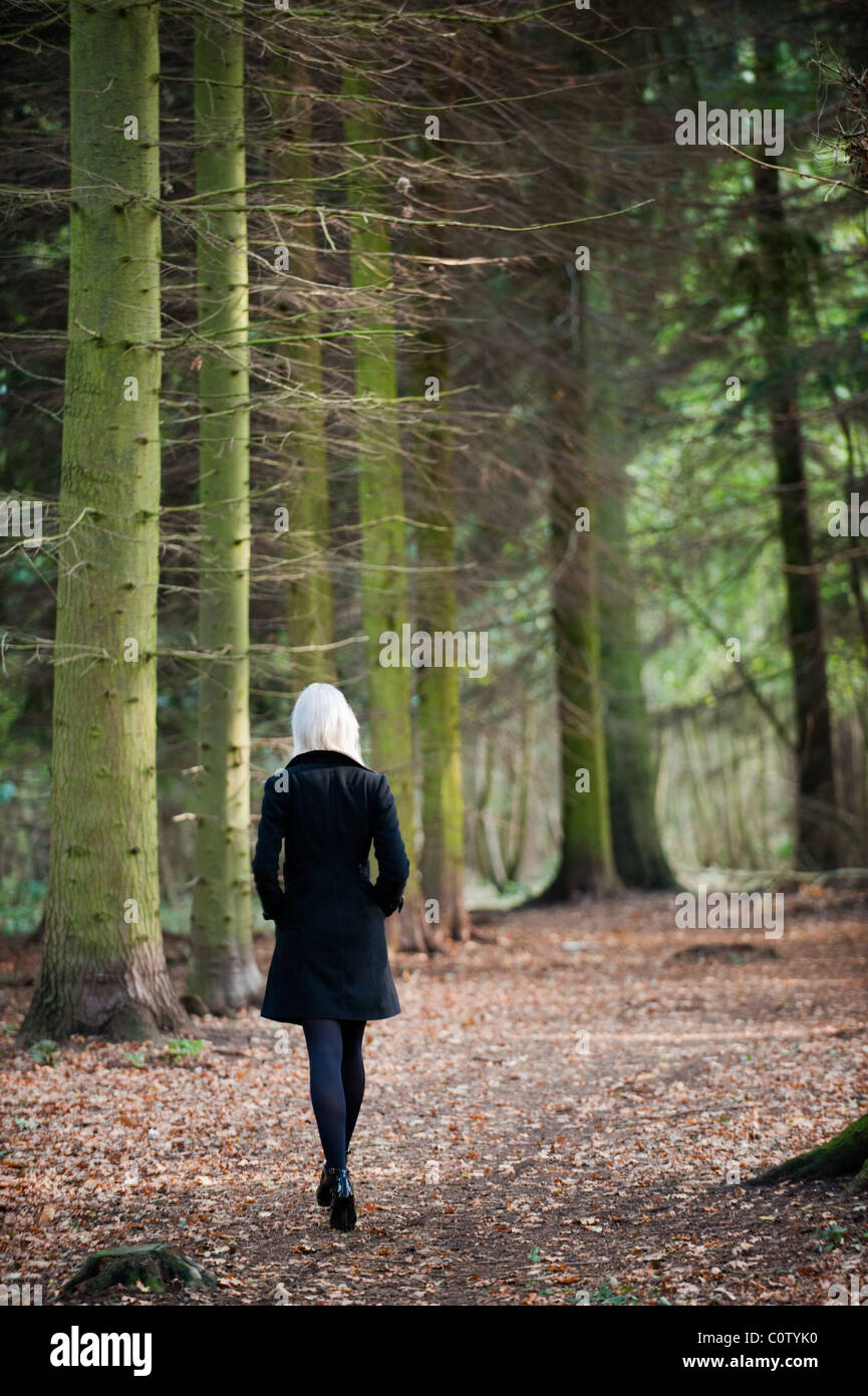 Joven Rubia modelo en negro stiletto zapatos y abrigo caminar solo a través de los bosques en otoño caen Foto de stock