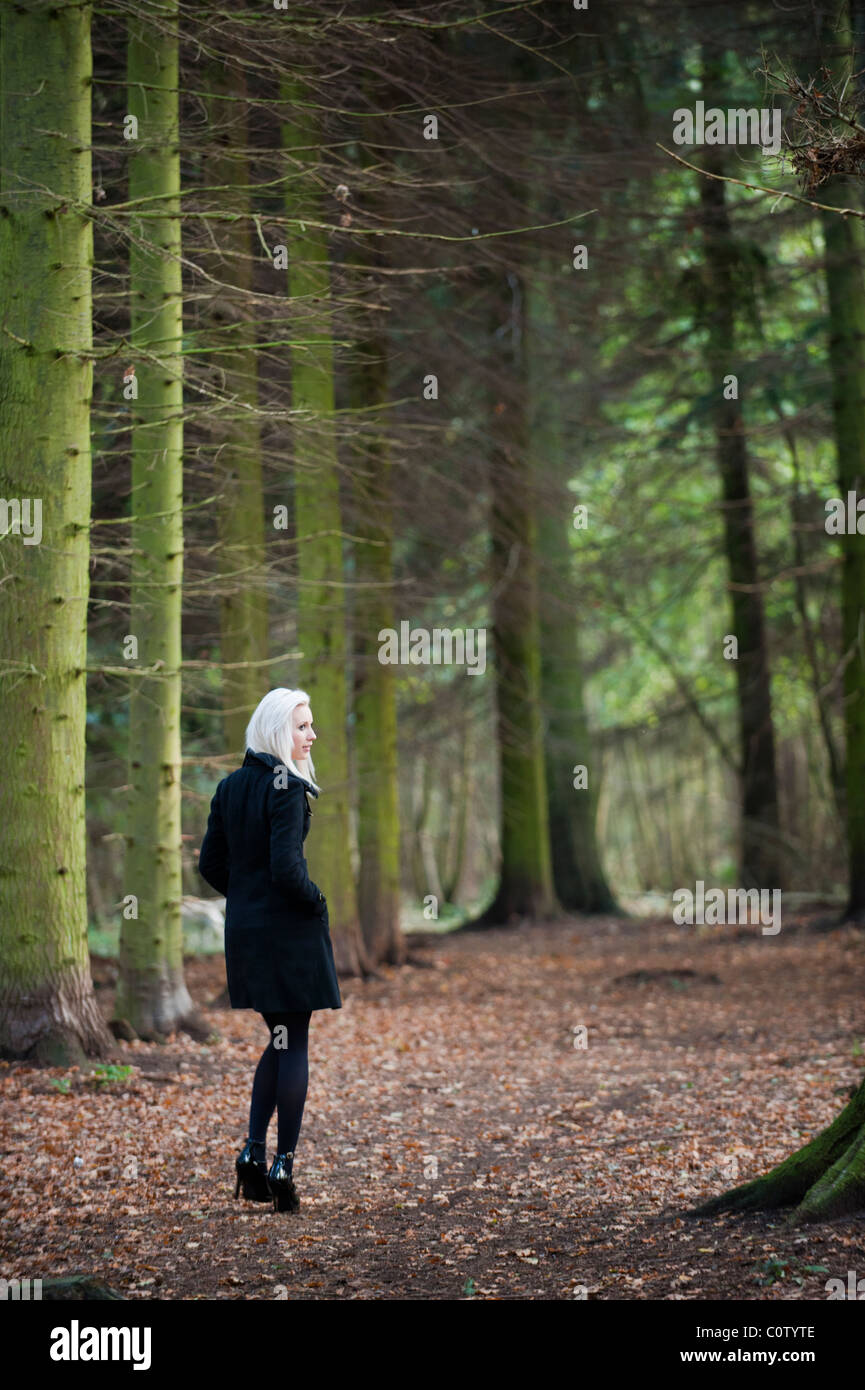 Joven Rubia modelo en negro stiletto zapatos y abrigo caminar solo a través de los bosques en otoño caen Foto de stock