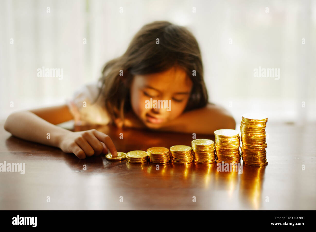 Invertir en oro. Chica con monedas de oro de chocolate apiladas. Foto de stock