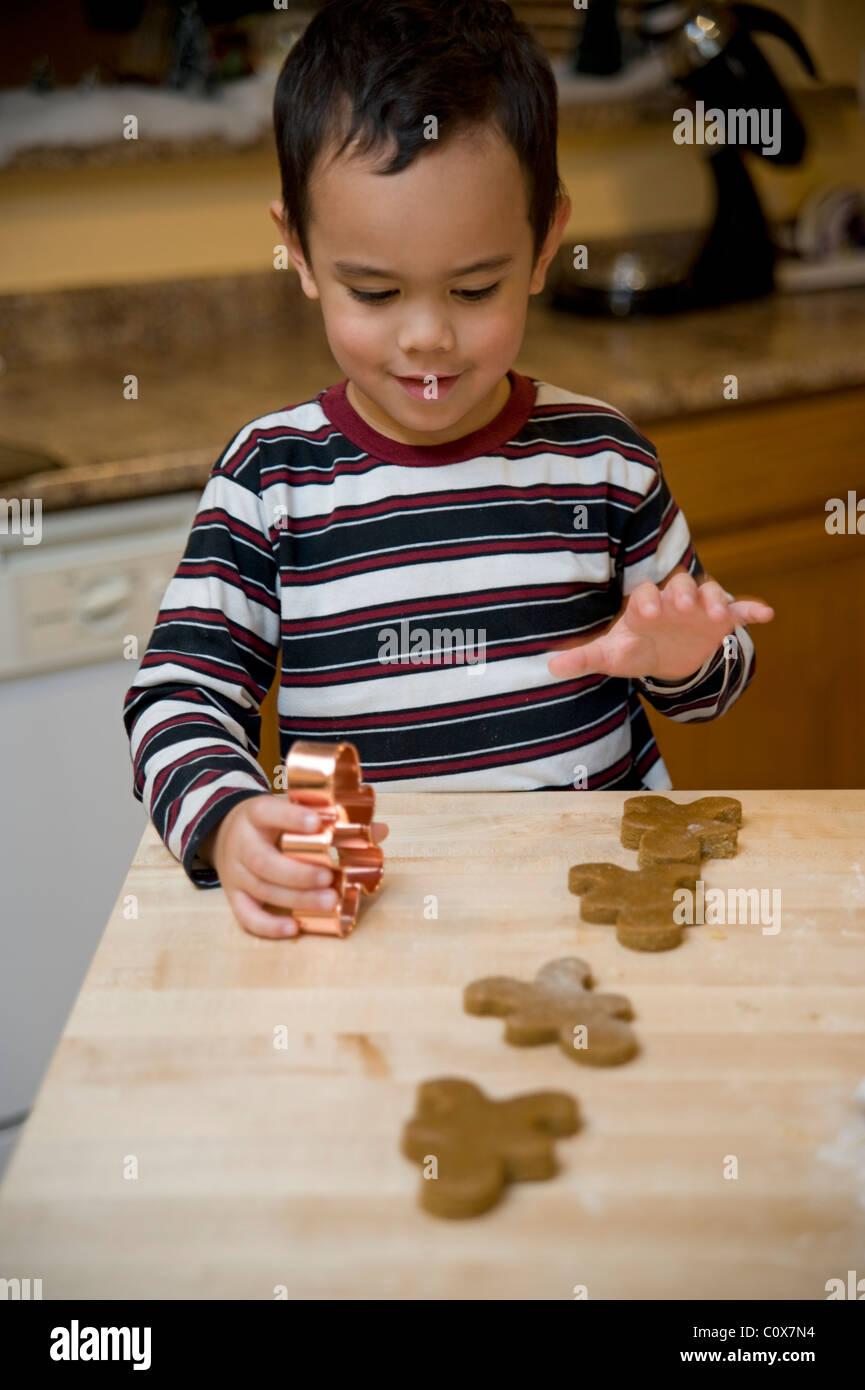 Un joven muchacho de raza mixta (Asiáticos y Caucásicos) ayuda a hornear galletas de jengibre en la cocina. Foto de stock