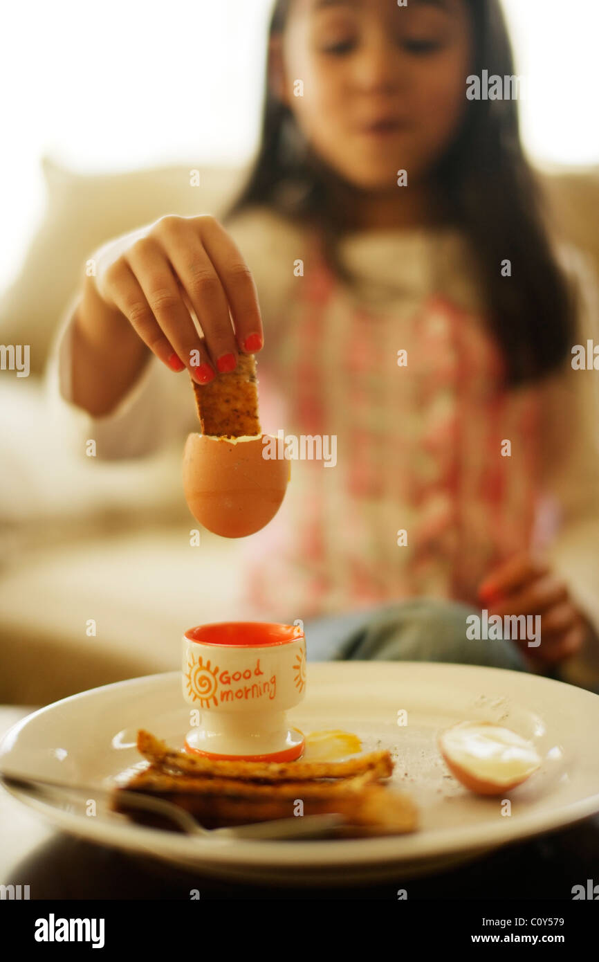 Chica come huevos con tostadas soldados para el desayuno Foto de stock
