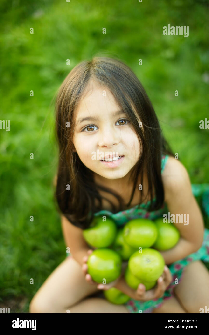 Niña de seis años se sienta sobre el césped y tiene manzanas verdes Foto de stock