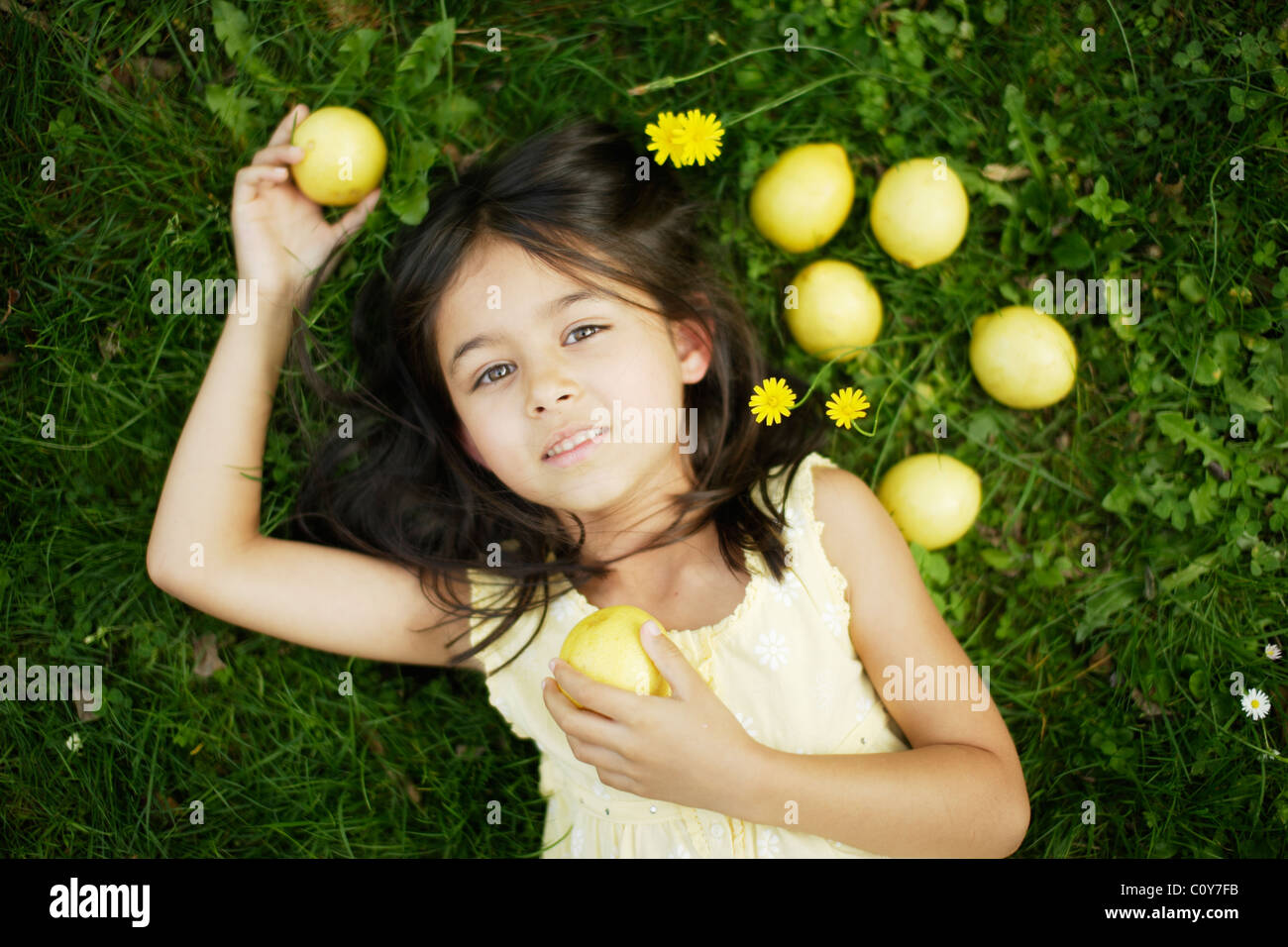 Niña de seis años se encuentra en la hierba con limones amarillos Foto de stock