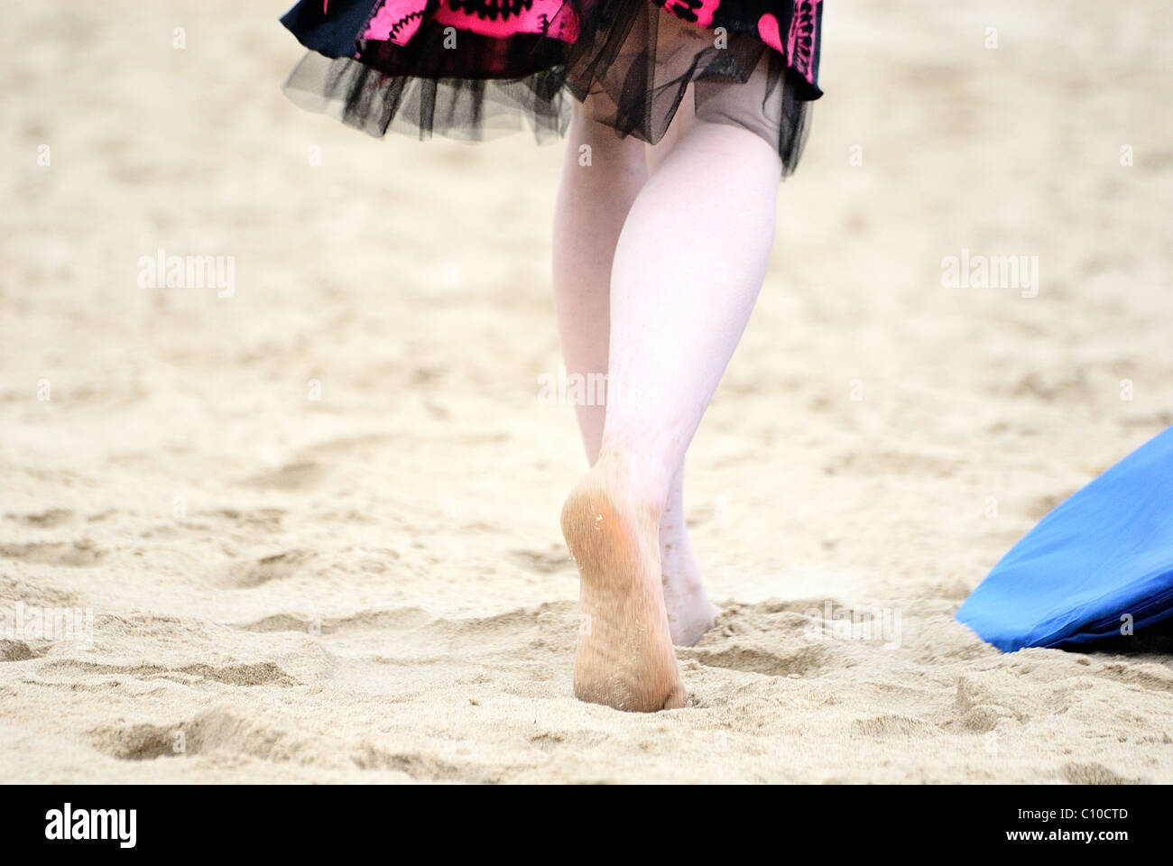 Un par de pies caminando por la playa en un vestido rosado y negro, caminando sobre la arena puedes ver la suela de un pie. Foto de stock