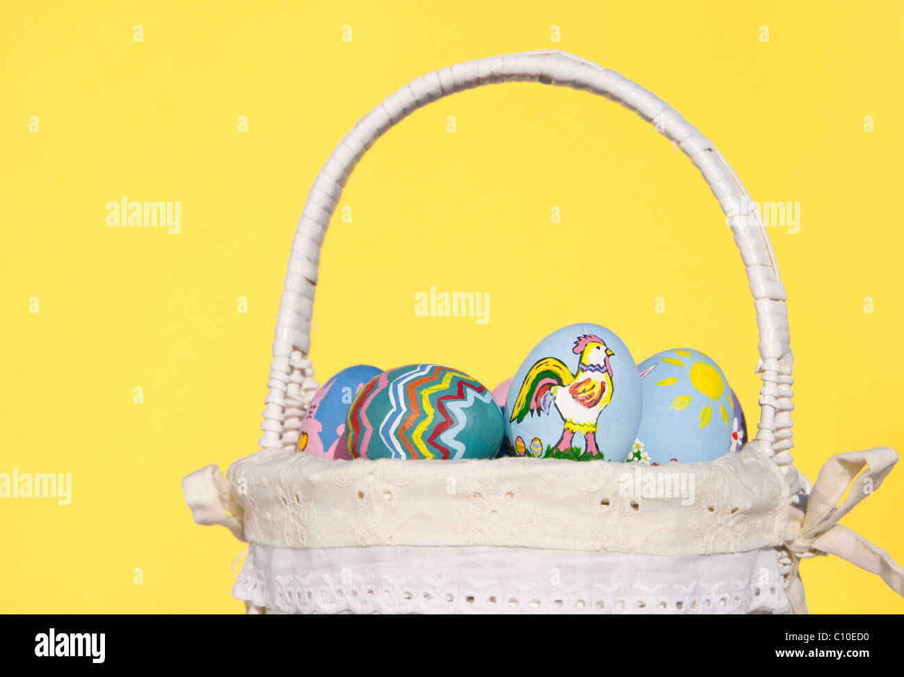 Canasta de mimbre llena de coloridos huevos de Pascua pintados a mano contra pascua fondo amarillo Foto de stock