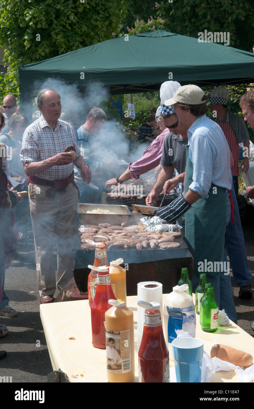 La cocción de los alimentos ,hamburguesas, salchichas, fuera, en la barbacoa en fiestas harting. fete celebrados anualmente en mayo en el sur de Harting, West Sussex, Reino Unido. Foto de stock