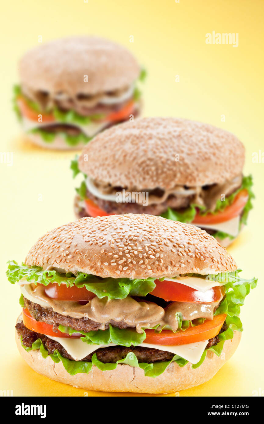 Tres deliciosas hamburguesas sobre un fondo amarillo Foto de stock