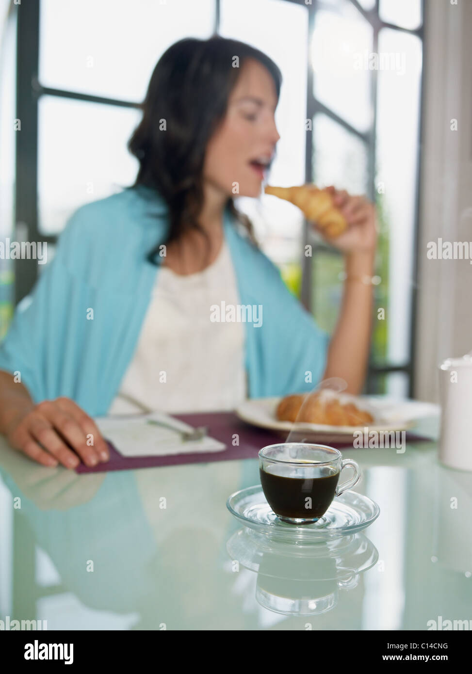 Mujer adulta media comiendo croissants en casa. De forma vertical, copie el espacio, centrarse en la taza de café Foto de stock