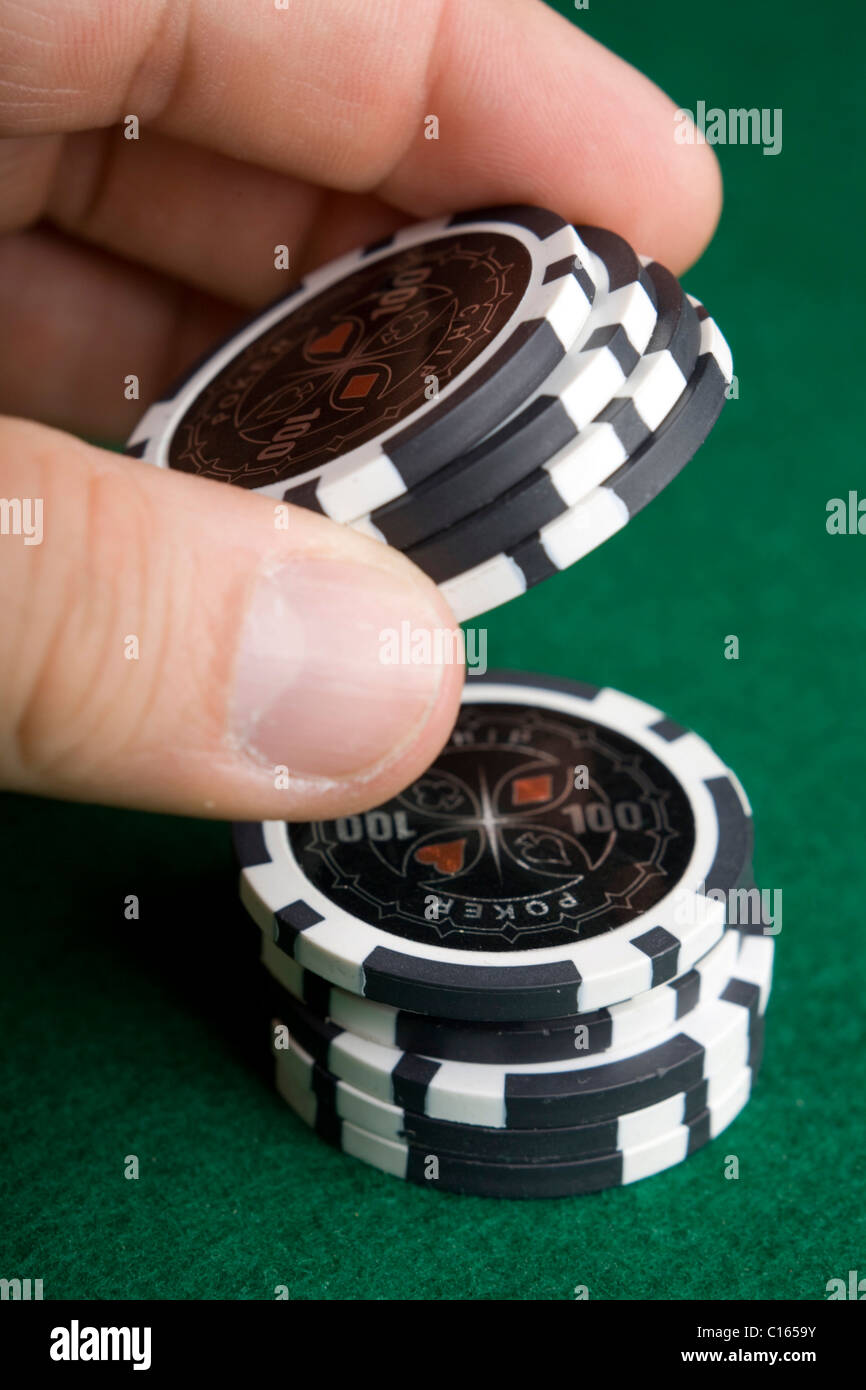 Alcanzando la mano negra de una pila de fichas de poker en fieltro verde Foto de stock