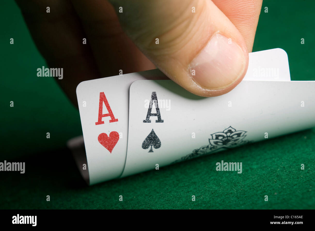 Mano levantando el borde de dos cartas, el as de corazones y el as de tréboles, en un juego de poker Foto de stock
