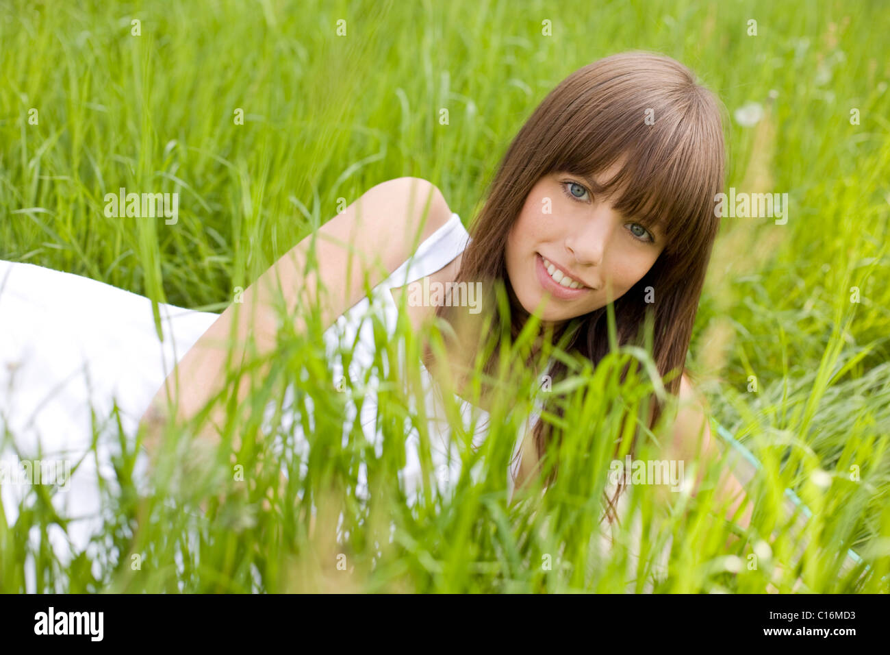 Joven mujer morena luciendo un vestido blanco, acostado en un prado, disfrutando del verano Foto de stock