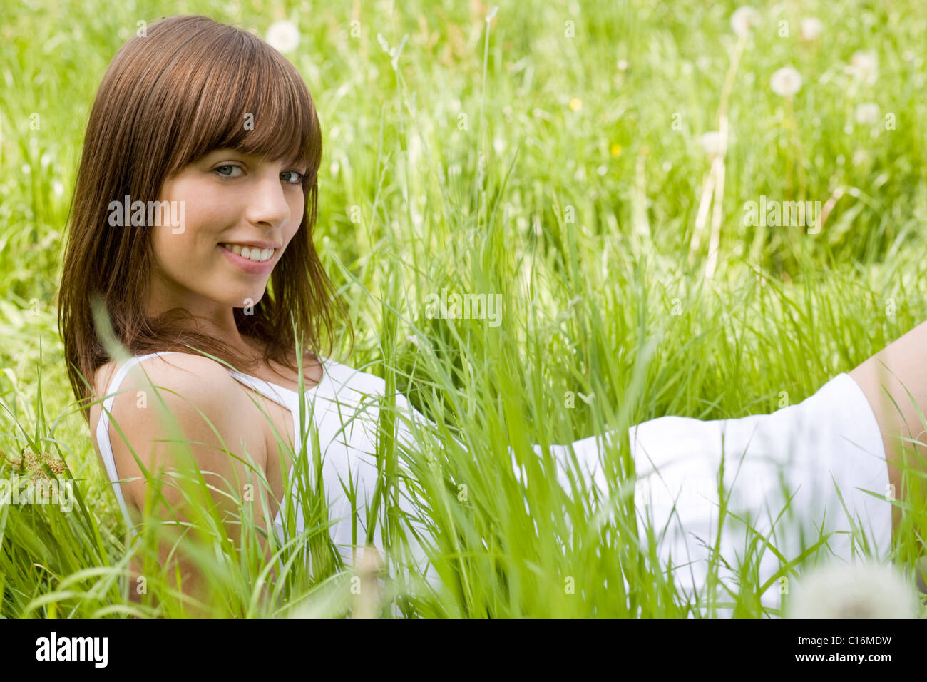 Joven mujer morena luciendo un vestido blanco, acostado en un prado, disfrutando del verano Foto de stock