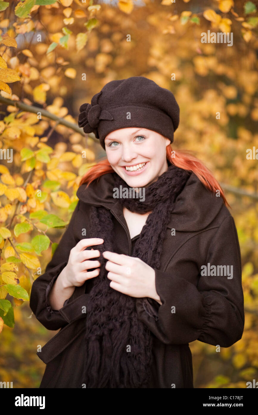 Rojo joven pelirroja mujer vistiendo un sombrero de lana y bufanda en un bosque otoñal Foto de stock
