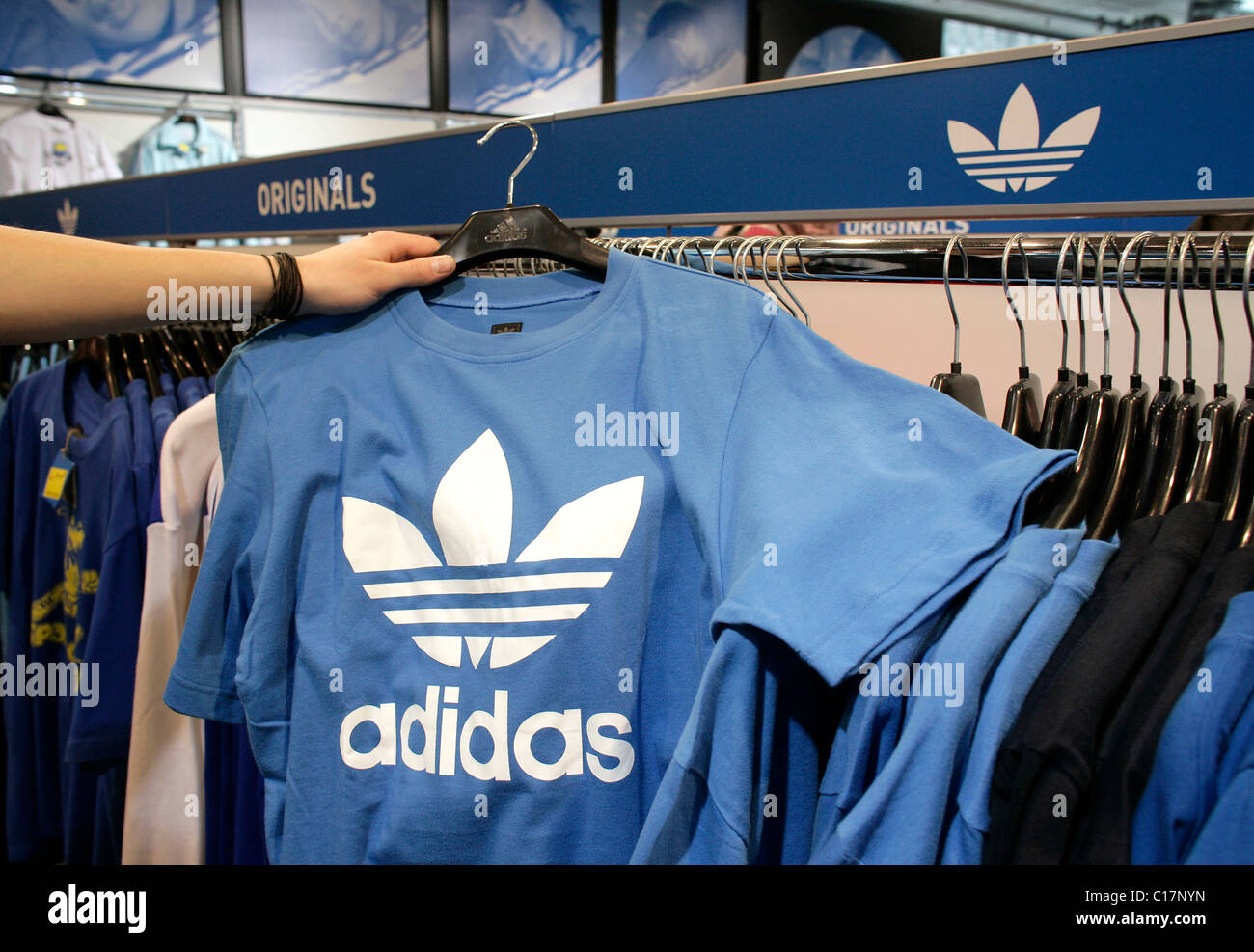 Un empleado mantiene una camiseta con el logotipo de adidas en una salida de la tienda adidas Salomon AG en Herzogenaurach, Baviera Fotografía de stock -