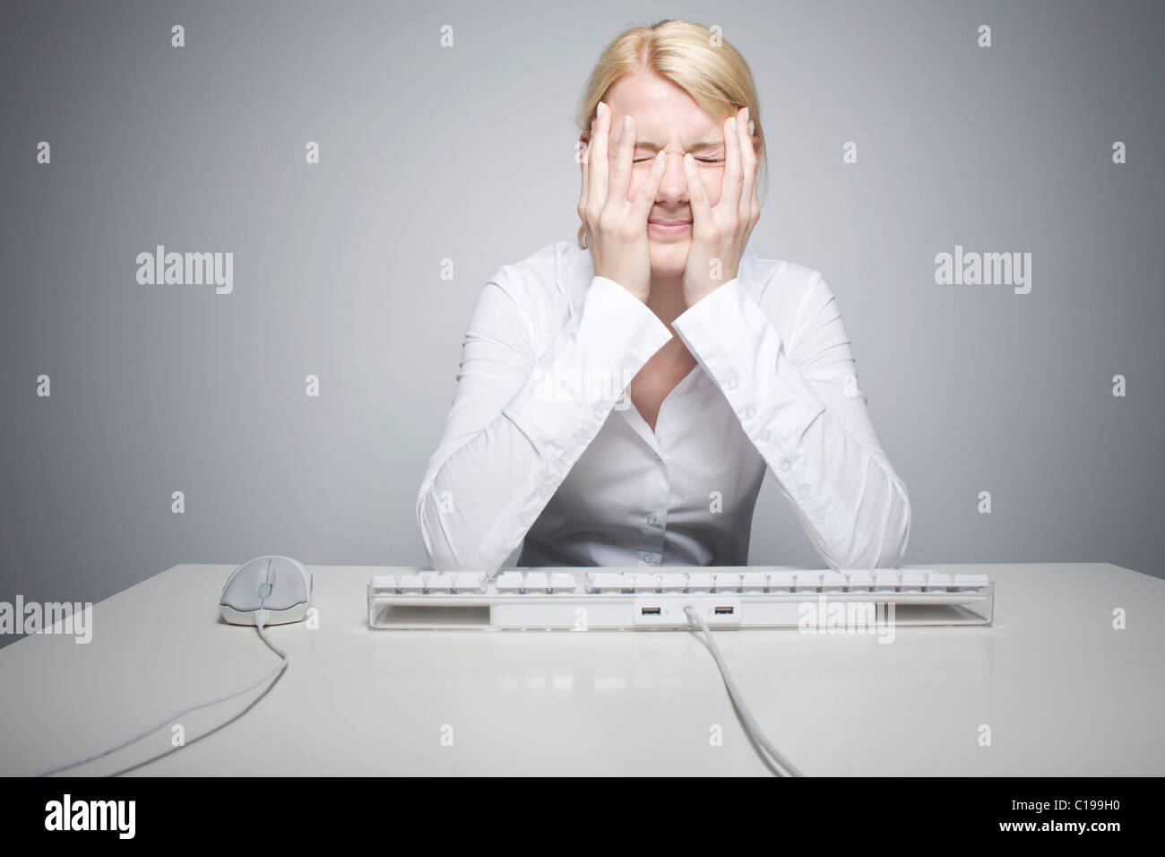 Mujer rubia joven sentado delante de un teclado de ordenador, desesperada Foto de stock