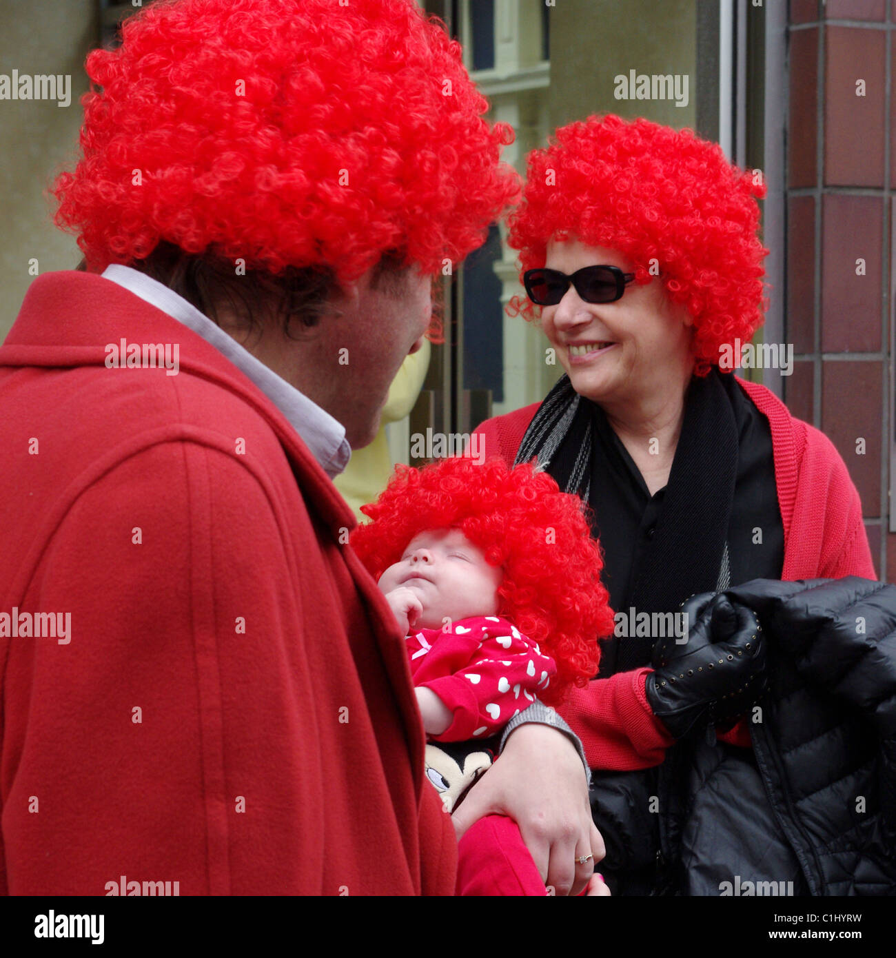 Pareja con bebé, todos vestidos de rojo de pelucas, reuniendo dinero para  alivio cómico Fotografía de stock - Alamy