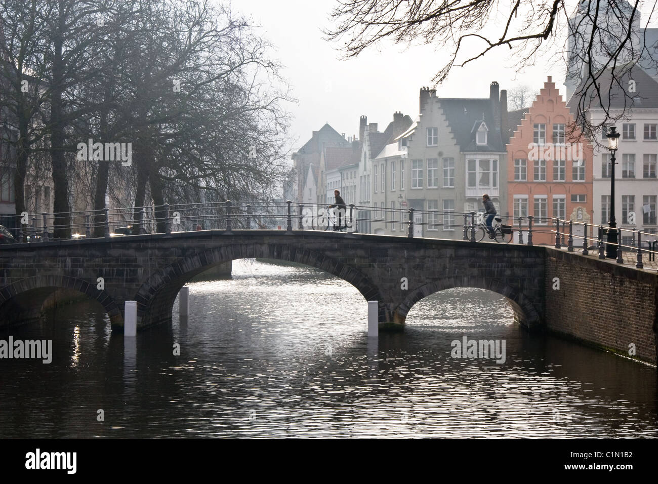 Los ciclistas en el puente sobre el canal, Misty mañana invernal, Brujas, Bélgica Foto de stock