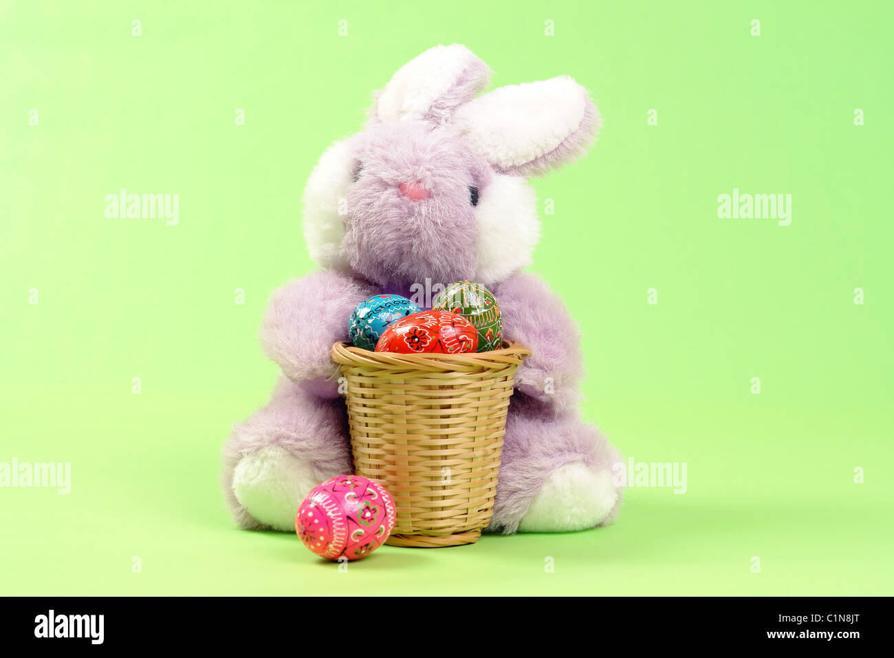 Conejito de Pascua sentado con madera canasta llena de huevos de Pascua sobre fondo verde claro Foto de stock