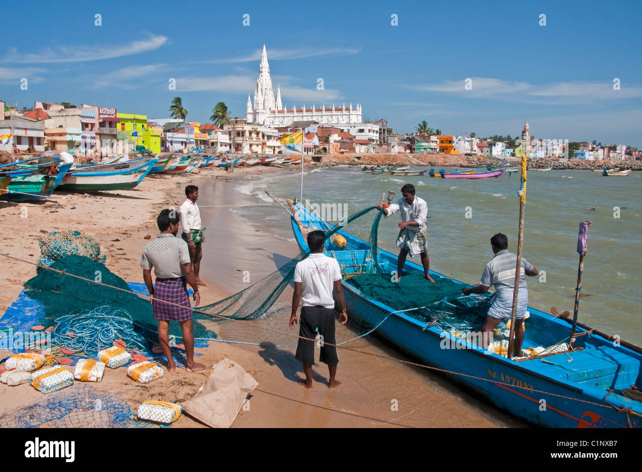 Los pescadores en la playa de Kanyakumari waterfront la preparación de redes con la Iglesia de Nuestra Señora de la Merced en segundo plano. Foto de stock