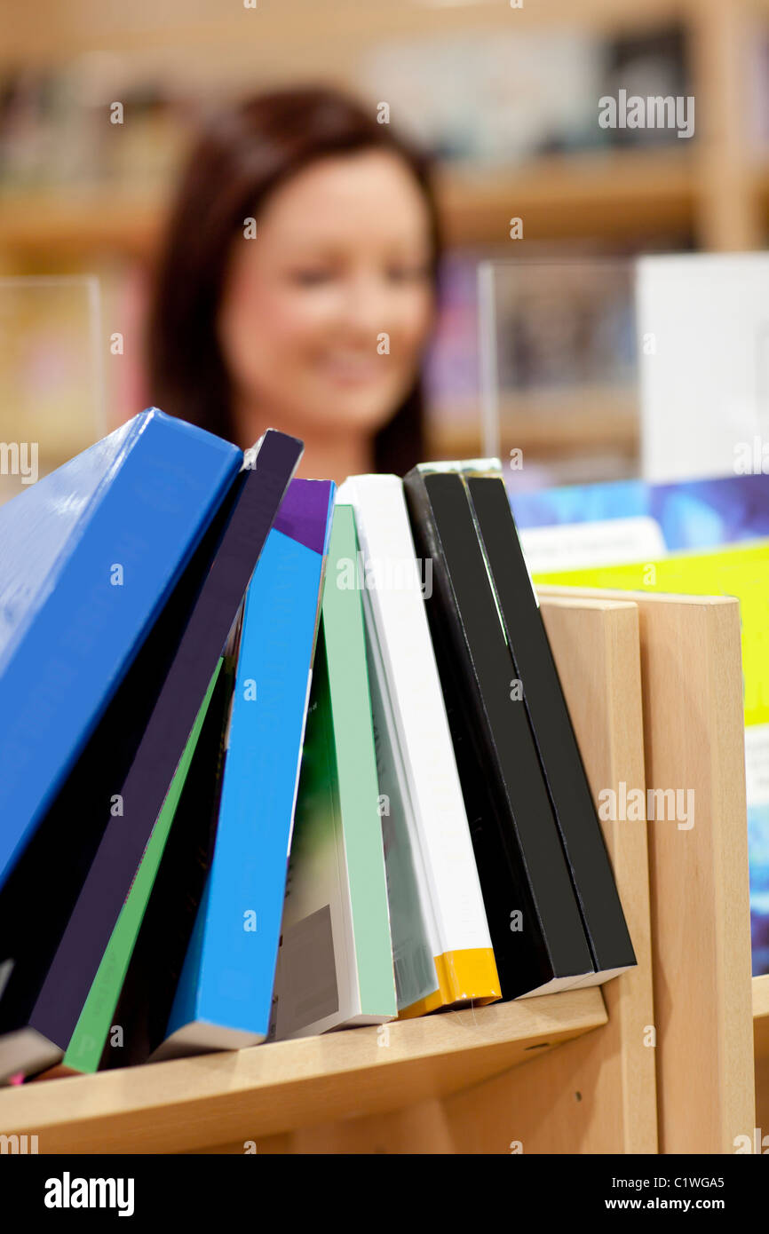 Close-up de una estantería de libros en una biblioteca con una clienta en el fondo Foto de stock