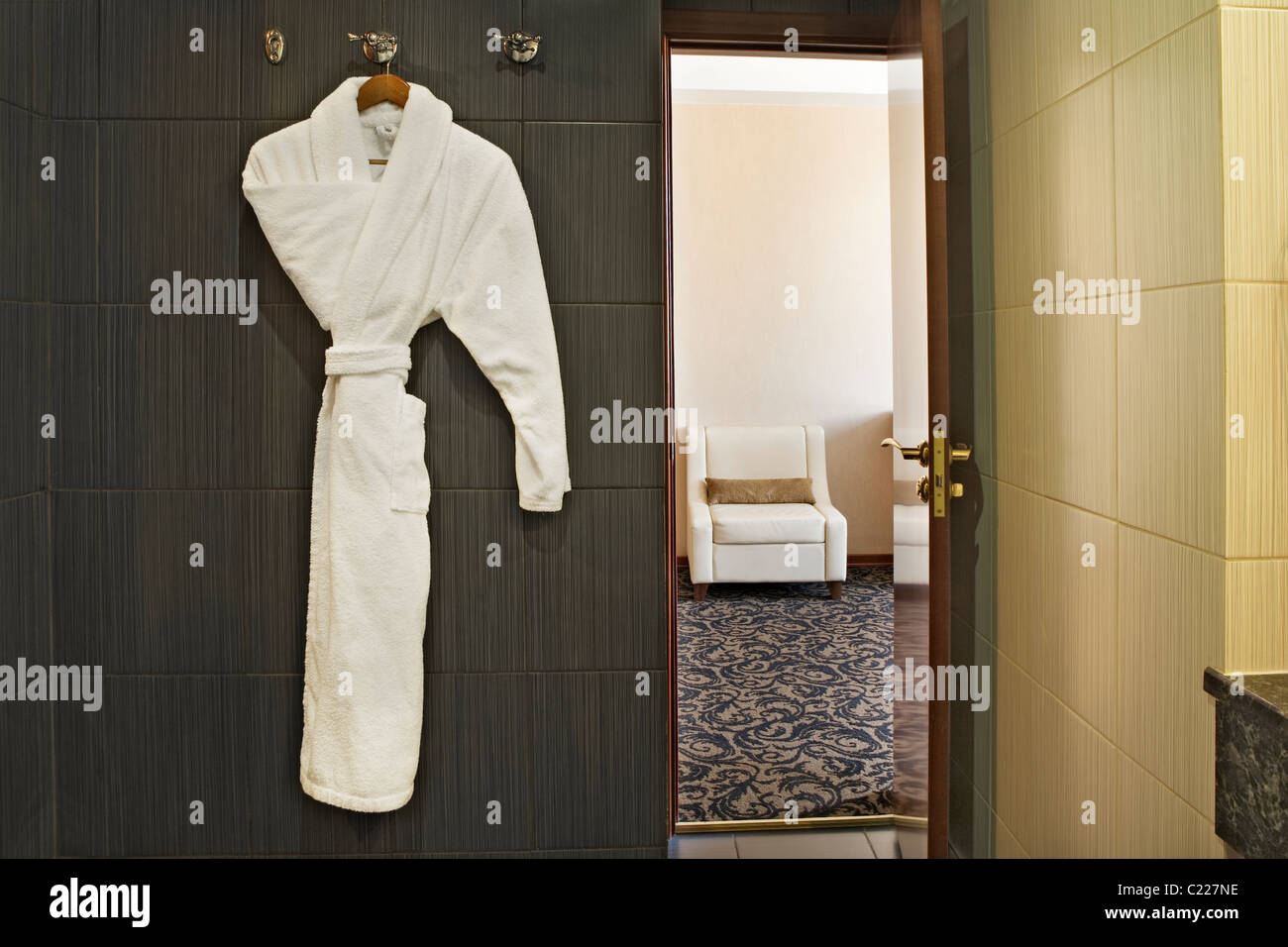 Interior de una habitación de hotel con una bata blanca de colgar y la puerta abierta con vistas a través de la habitación de al lado Foto de stock