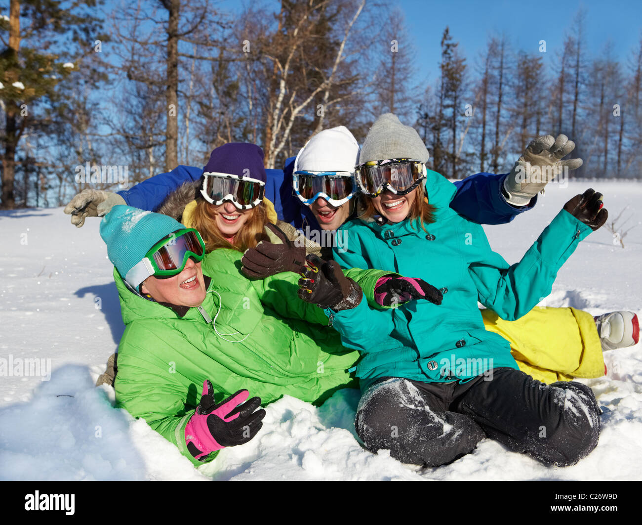 Retrato de cuatro adolescentes riéndose en gafas de esquí sentado en la nieve Foto de stock