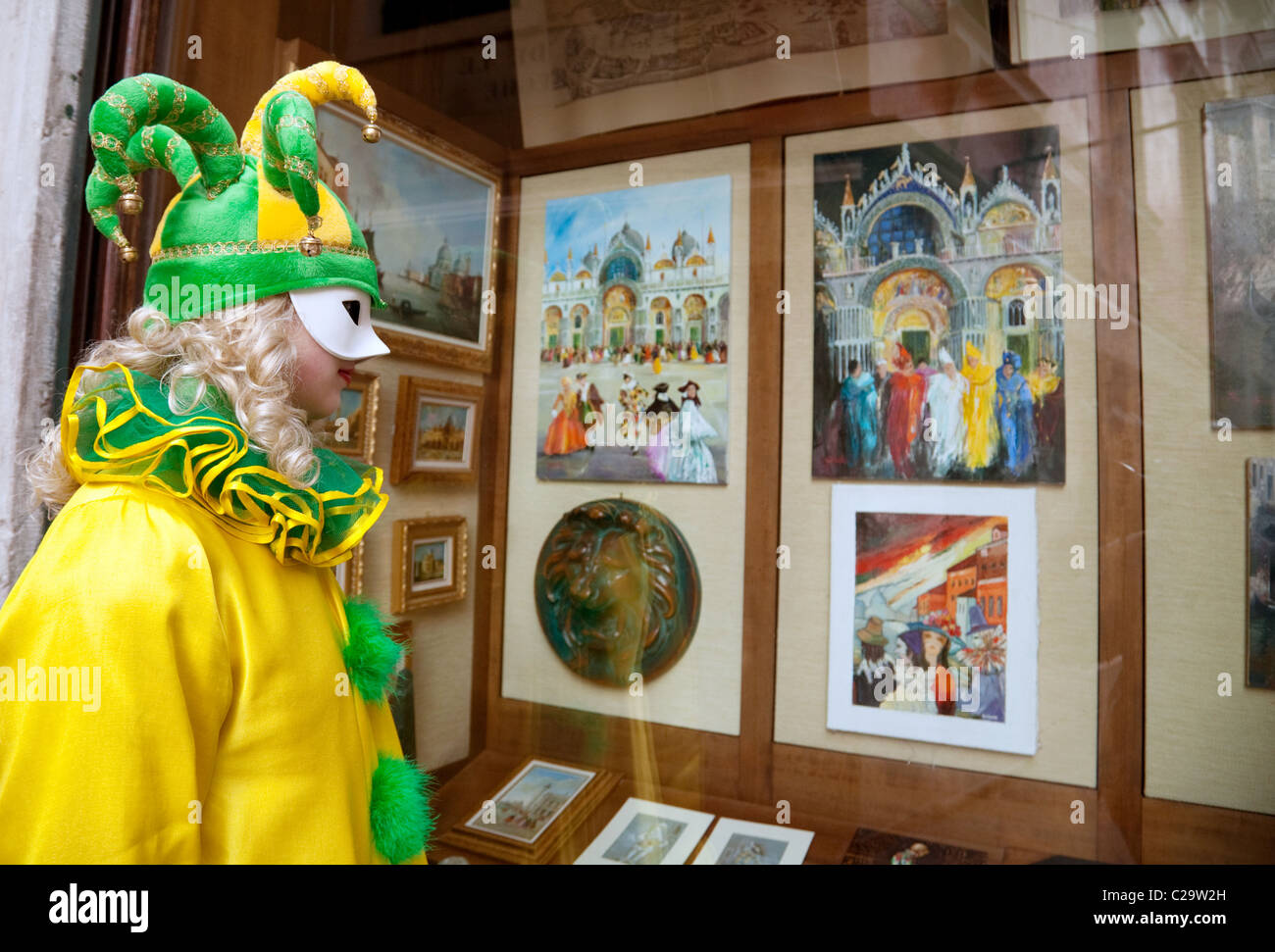 Una chica en Disfraz de payaso mira pinturas de Venecia en una galería de cristal en el Carnaval de Venecia, Italia Foto de stock