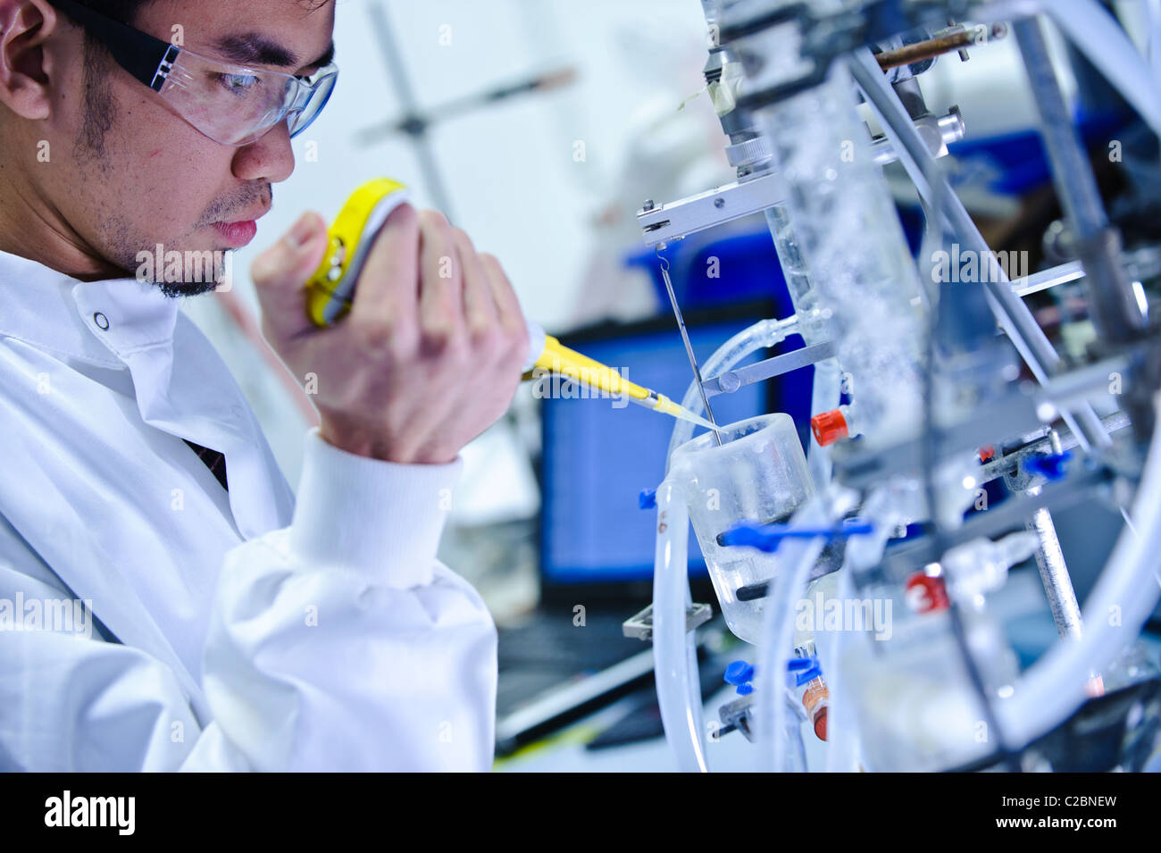 Los jóvenes asiáticos científico masculino vistiendo gafas transparentes y ciencia blanca cubra mirando el tubo de vidrio de aparatos en el laboratorio de ciencias Foto de stock